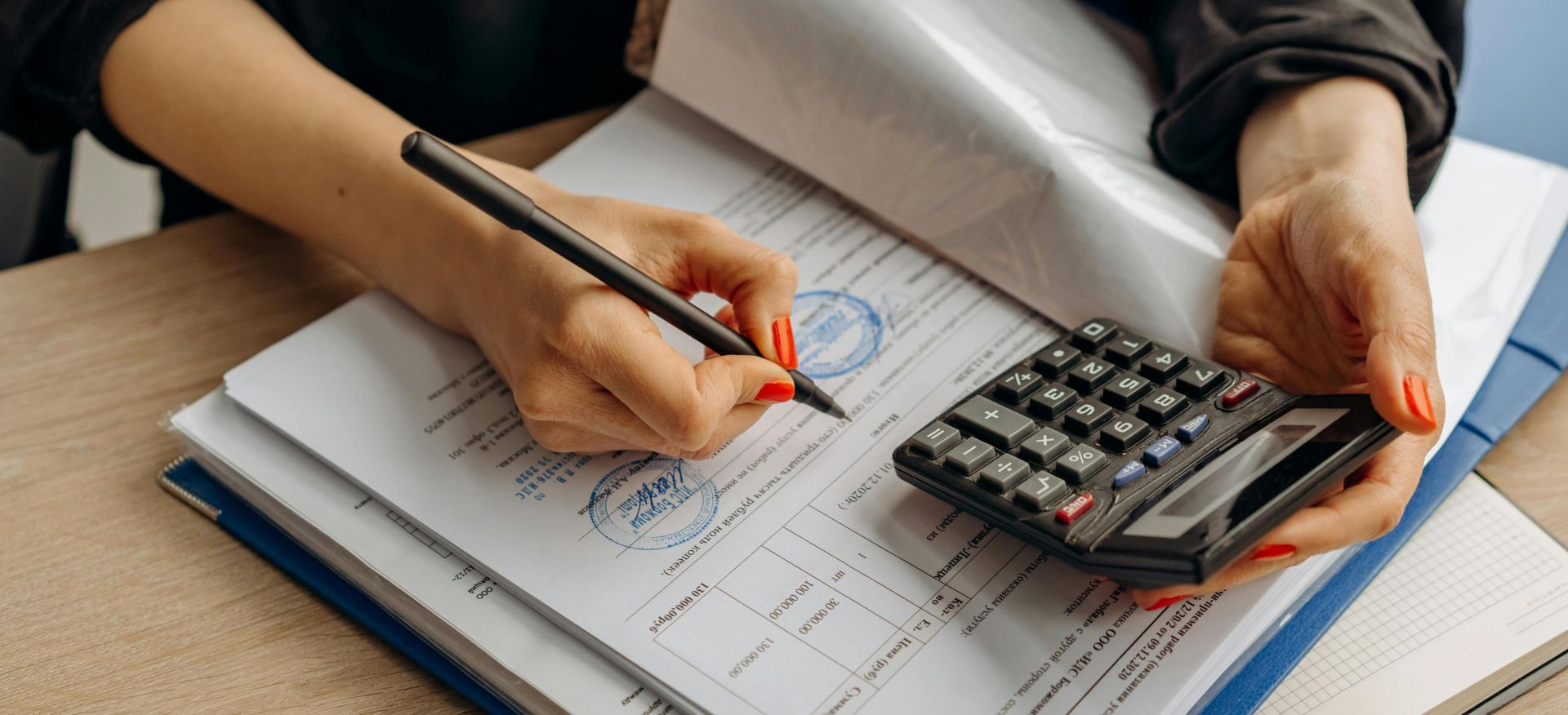 An accountant using a calculator and signing paperwork, showcasing financial analysis.